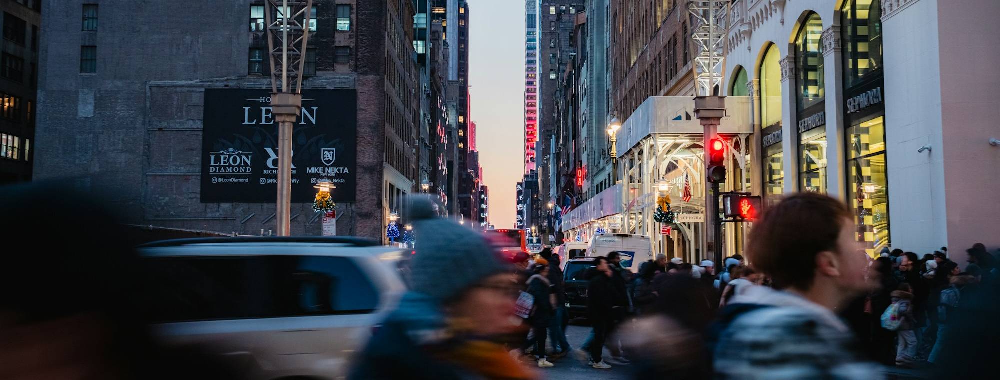 People crossing a busy Midtown Manhattan street at dusk