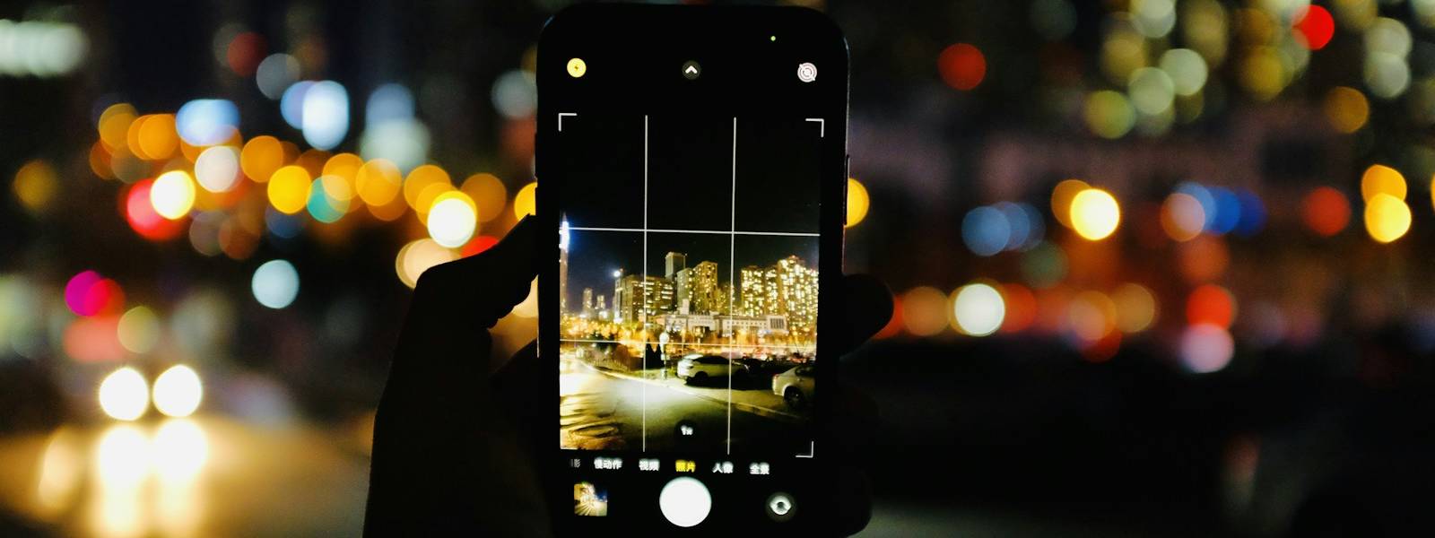 Hand holding a phone camera up to a city skyline at night